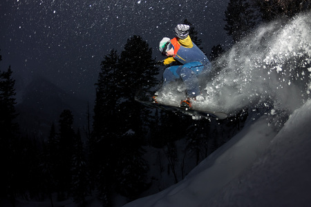 freerider snowboarder jumping at night with a springboard in the forest.