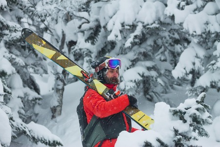 Portrait young man ski goggles holding ski in the mountains.