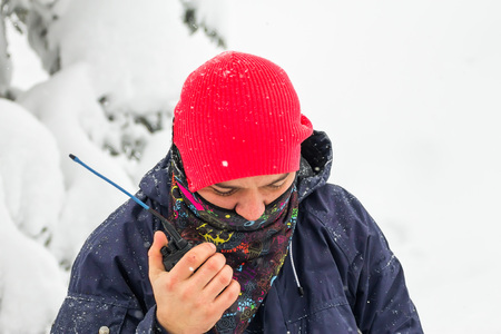 Freerider man talking on a portable radio set in a snowy forest.