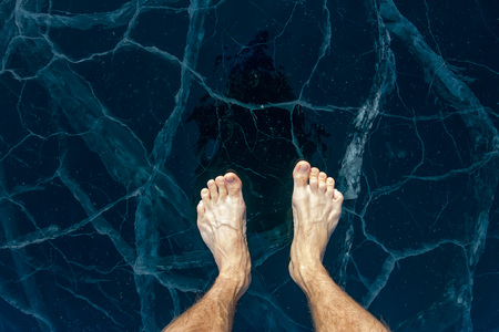 Barefooted male feet stand on the blue ice of Lake Baikal, in cracks.の写真素材