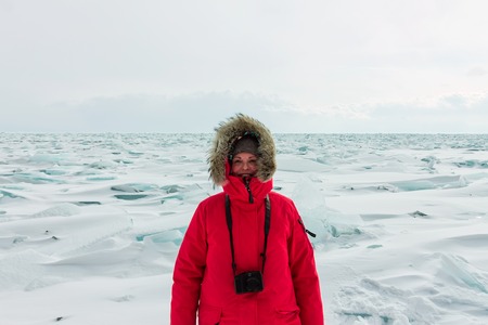 Portrait of a woman in a parka jacket with a fur hood in a snowy Baikal in hummocks.