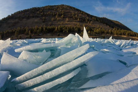dawn in the blue hummocks of ice lake baikal, in a snowy field in winter on a journey.の写真素材