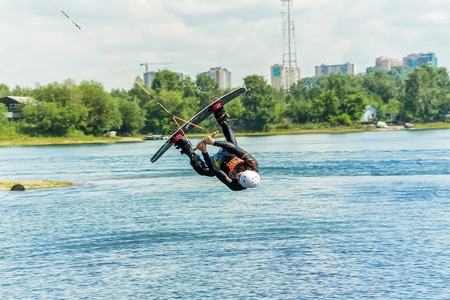 wakeboarder jumps from a springboard behind a rope and makes a wave on the water.