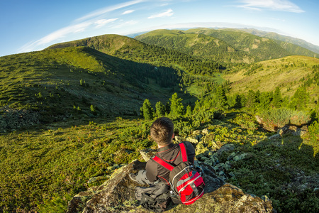 young man with a backpack sits on a rock in the mountains view.の写真素材