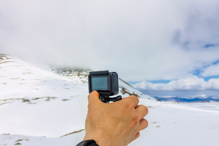 Hand holding action camera action camera stands on a tripod against the backdrop of the mountains.の写真素材