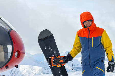 Snowboarder freerider is standing at the helicopter in the snowy mountains in winter under the cloudsの写真素材