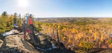 Couple of tourists with backpacks man and woman standing on a rock in autumn forest panoramaの写真素材