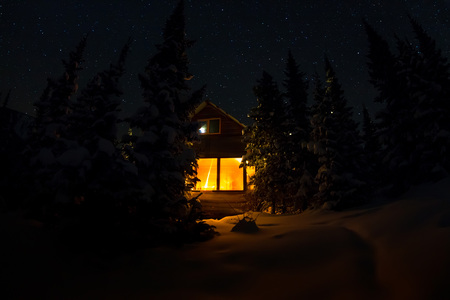 Light from the window of a forest hut under the night sky of the milky way in the winter forestの写真素材