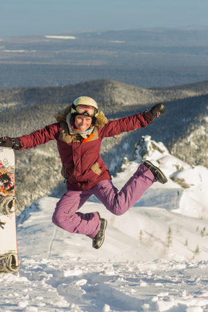 Snowboarder girl freerider is jump in the snowy mountains in winter under the cloudsの写真素材