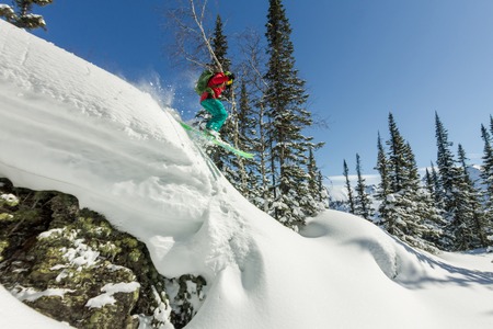 Freerider skier jumps from a rock of snow in trees in the mountainsの写真素材