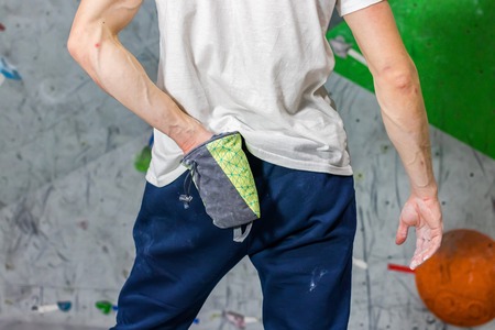 Rock climber man shoved his hands into a bag of magnesia powder behind his back in the boulder hall