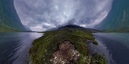 Black mountains in rain clouds, the foot covered with stones and green grass. Wide angle panorama