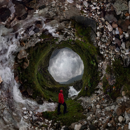 man in red stands under waterfall on black rock in mountains on cloudy rainy day.. . Tiny little...