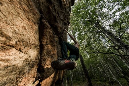 Rock climber climbs bouldering on a cliff on forest. Low angle of strong rock climbing man hanging free on rock with sunflareの写真素材