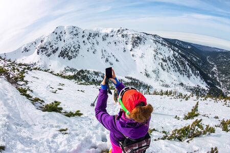 Woman hikeing in the snowy mountains with a phone and snowshoes. and backpack