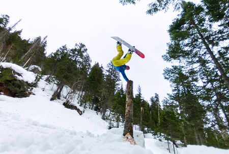 Snowboarder freerider standing on a dry log in a jump from a snow ramp in a background of forest and mountains.の写真素材