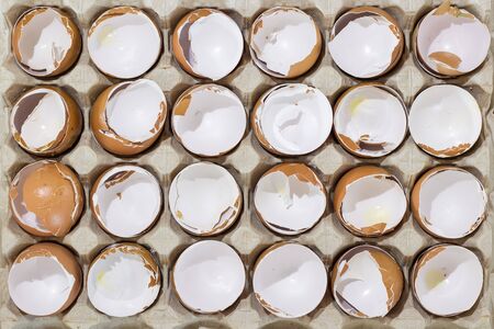 Flat view of a box with broken eggshell brown chicken eggs, background texture pattern.