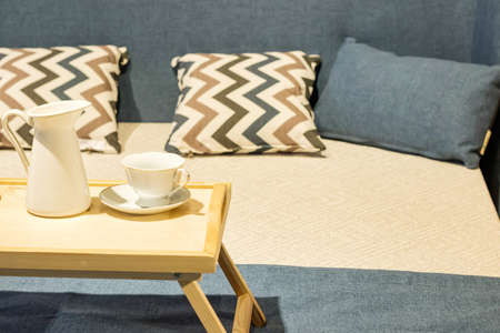wooden tea table stands on the bed with cups. Bed with pillows and blue duvet and wooden chest of...