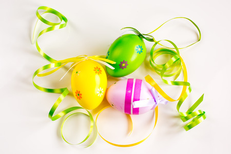 Three multi colored Easter eggs, green and yellow ribbons still life close upの写真素材