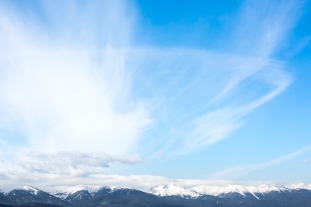 Snow covered mountain peaks and blue sky with clouds backgroundの写真素材
