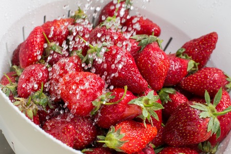 Freezed drops of water over the ripe strawberries rinsed with water in the white colander