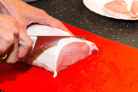 Cutting raw meat pieces on the red board with knifeの写真素材