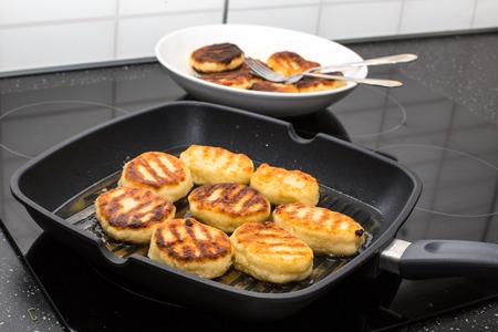Traditional homemade Russian sweet syrniki cottage cheese pancakes cooking in the frying pan and a plate behind itの写真素材