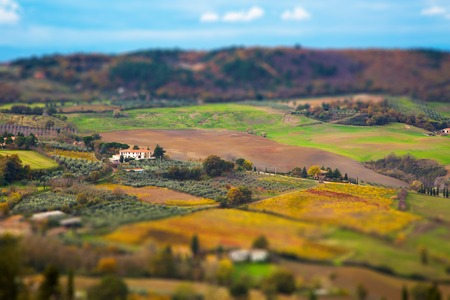 Beautiful colorful autumn Tuscany panoramic landscape with fields, trees and houses,  Italy and blue sky. tilt shift effectの写真素材