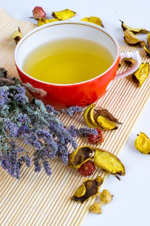 Herbal tea in red cup, dry marjoram herbs and dry flower petals on bamboo mat backgroundの写真素材