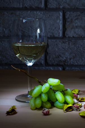 Lightened glass of white wine and grapes on wooden table and gray bricks backgroundの写真素材