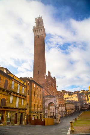Tower Torre del Mangia in Siena, Italy in the morning fog on the blue cloudy sky
