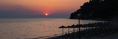 Tropical beach umbrellas, sun and colorful sunset sky panorama. Summertime vacation concept.の写真素材