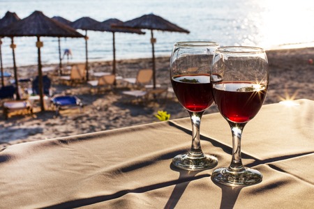 Two glasses with red wine with sun reflection, sea, sunset on beach at the background. Summertime vacation conceptの写真素材