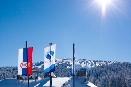 Kopaonik, Serbia - January 19, 2016: Serbian and ski resort flags on snowy mountain with trees background and sun in the corner. Place for textのeditorial素材