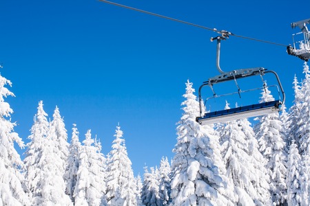 Ski resort image with empty chair lift, blue sky and white snowy pine trees at winter sunny dayの写真素材