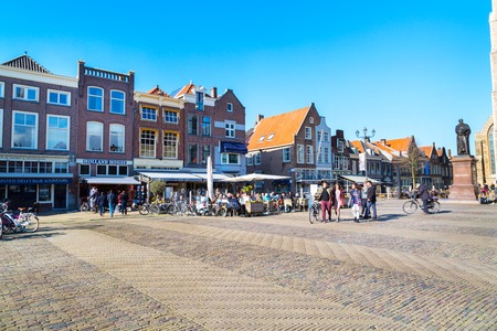 Delft, Netherlands - April 8, 2016: Colorful street view with traditional dutch houses on the square, bicycles, people walking in downtown of popular Holland destinationのeditorial素材