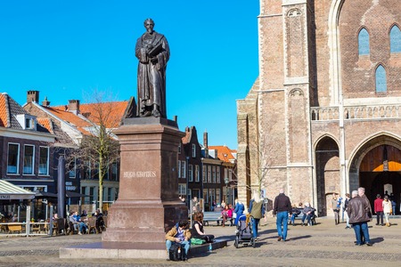 Delft, Netherlands - April 8, 2016: Colorful street view with statue of Hugo Grotius, Nieuwe Kerk or New Church entrance, traditional dutch houses on the square, people walking in downtown of popular Holland destinationのeditorial素材
