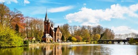 Bruges, Belgium - April 10, 2016: Minnewater lake panorama, reflection of gothic building and people in cafe near Castle de la Faille, cloudy blue sky, Bruges, Belgiumのeditorial素材