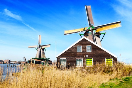 Old windmill in Zaanse Schans, traditional village in Netherlands, North Holland, high grass, blue cloudy skyの写真素材