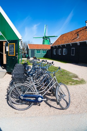Zaanse schans, Netherlands - April 1, 2016: Bikes for rent, windmill in Zaanse Schans, traditional village, Netherlands, North Holland, green houses against blue cloudy skyのeditorial素材
