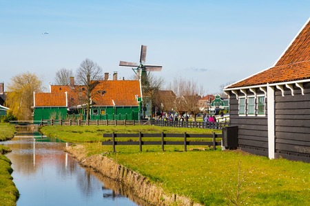 Zaanse schans, Netherlands - April 1, 2016: Zaanse Schans, North Holland, traditional village, tourists, green houses and windmills against blue cloudy skyのeditorial素材