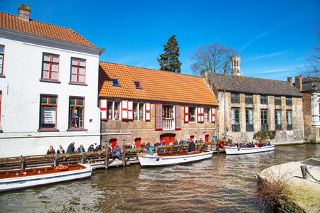 Bruges, Belgium - April 10, 2016: Scenic cityscape with medieval houses, cruise boat station with tourists and canal in Bruges, Belgiumのeditorial素材
