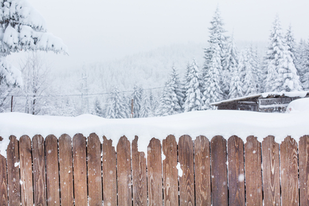 Rural winter scene. Snow covered wooden fence and snowy trees on backgroundの写真素材