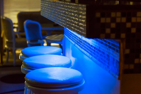 Empty bar stools along bar Illuminated in blue purple lightの写真素材