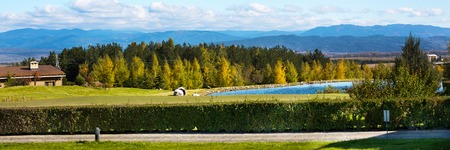 Panorama of Beautiful autumn Landscape view of the lake, colorful trees, wooden chalet and mountains backgroundの写真素材