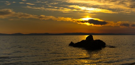 Golden sunset over sea in Greece coast with clouds and stone silhouette panoramaの写真素材