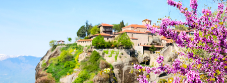 Panorama banner with blurred Great Meteoro Monastery in Meteora rocks, snowy mountains and branch of pink cherry blossomの写真素材