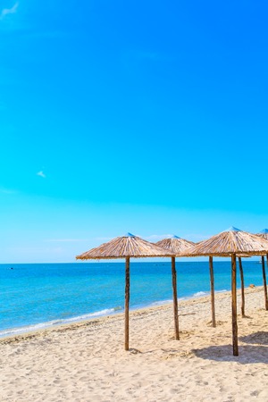 Row of wooden umbrellas at sandy beach, sea and blue sky background, Greece.の写真素材