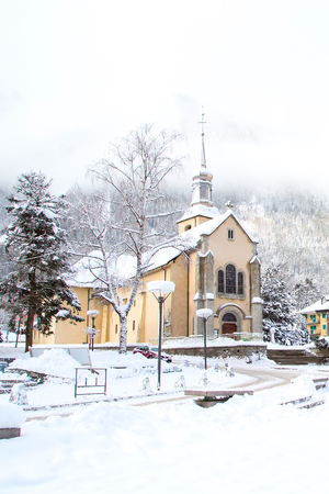 Church in Chamonix town, France, French Alps in winter with foggy snow mountains at the backgroundの写真素材