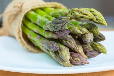 Bunch of fresh asparagus on wooden table and white plate, healthy foodの写真素材